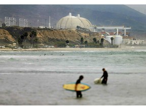 FILE - In this June 7, 2013 file photo surfers stand in water in front of the shuttered San Onofre Nuclear Generating Station in San Onofre, Calif. The Nuclear Regulatory Commission is fining Southern California Edison $116,000 for violations in its handling of nuclear canisters at the facility. The decision announced Monday, March 25, 2019, in an online town hall meeting involves the transfer of radioactive nuclear waste containers from cooling pools to safer bunkers. The Orange County Register reports Southern California Edison indicated it would accept the penalty.