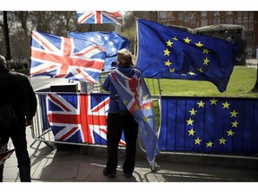 An anti-Brexit supporter stands by European and British Union flags placed opposite the Houses of Parliament in London, Monday, March 18, 2019. British Prime Minister Theresa May was making a last-minute push Monday to win support for her European Union divorce deal, warning opponents that failure to approve it would mean a long -- and possibly indefinite -- delay to Brexit. Parliament has rejected the agreement twice, but May aims to try a third time this week if she can persuade enough lawmakers to change their minds.