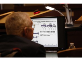 Former U.S. Sen. Harry Reid sits in front of a monitor showing instructions for an exercise band in court Tuesday, March 26, 2019, in Las Vegas. A jury in Nevada heard opening arguments Tuesday in Reid's lawsuit against the maker of a flexible exercise band that he says slipped from his hand while he used it in January 2015, causing him to fall and suffer lasting injuries including blindness in one eye.