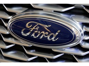 FILE- This Feb. 15, 2018, file photo shows a Ford logo on the grill of a car on display at the Pittsburgh Auto Show. Ford Motor Co. is repackaging a previously announced manufacturing investment in the Detroit area and now says it will spend $900 million and create 900 new jobs over the next four years. Most of the new workers will build a new generation of electric vehicle at Ford's existing factory in Flat Rock, Michigan, south of Detroit, which will see an $850 million investment.