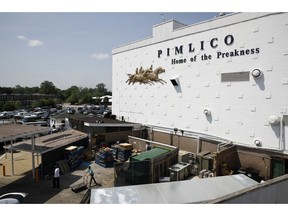 FILE - In this May 15, 2018 file photo, people walk outside of a building at Pimlico Race Course as preparations take place for the Preakness Stakes horse race, in Baltimore. Baltimore has ratcheted up a bitter dispute with the owners of the historic racetrack in an effort to seize a nearly 150-year-old course and block the move of one of America's premier horse races out of the city where it was first run in 1873. Under state law, the Preakness Stakes - the middle jewel of the Triple Crown of thoroughbred horse racing - can be moved to another track in Maryland "only as a result of a disaster or emergency." But the Canada-based development company that owns and operates the rundown Pimlico Race Course has made it abundantly clear that it wants to move the storied race out of the city.