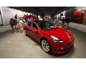 FILE- In this July 6, 2018, file photo, prospective customers confer with sales associates as a Model 3 sits on display in a Tesla showroom in the Cherry Creek Mall in Denver. Tesla is suffering one of its worst sell-offs of the year after announcing it would begin closing all of its stores in favor of selling its electric cars exclusively online. The goal is to allow Tesla to lower the price of its Model 3, the vehicle that CEO Elon Musk envisions as the company's first mass-market vehicle.