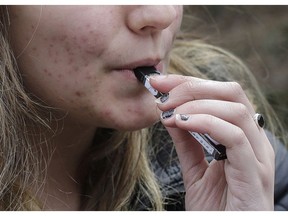 FILE - In this April 11, 2018, file photo, a high school student uses a vaping device near a school campus in Cambridge, Mass. U.S. health regulators are moving ahead with a plan to keep e-cigarettes out of the hands of teenagers by restricting sales of most flavored products in convenience stores and online.