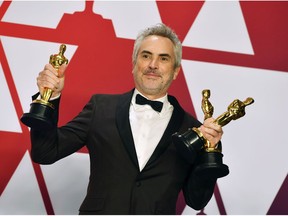 FILE - In this Sunday, Feb. 24, 2019, file photo, Alfonso Cuaron poses with the awards for best director for "Roma," best foreign language film for "Roma," and best cinematography for "Roma" in the press room at the Oscars at the Dolby Theatre in Los Angeles. "Roma" may not have won the best picture Oscar this year, but it came close enough to make some of Hollywood's top players worry about Netflix's infiltration of their most prestigious award.