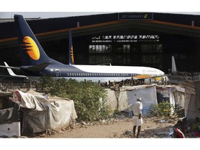 A man stands next to his shanty as Jet Airways aircraft is seen parked at a hanger at Chhatrapati Shivaji Maharaj International Airport in Mumbai, Monday, March 25, 2019. The chairman of India's private Jet Airways has quit amid mounting financial woes forcing the airline to suspend operations on 14 international routes with more than 80 planes grounded.