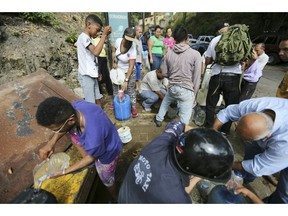 People collect water from an open pipeline during rolling blackouts, which affects the water pumps in people's homes and apartment buildings, in Caracas, Venezuela, Monday, March 11, 2019. The blackout has intensified the toxic political climate, with opposition leader Juan Guaido blaming alleged government corruption and mismanagement and President Nicolas Maduro accusing his U.S.-backed adversary of sabotaging the national grid.