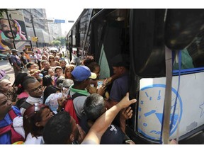 People jockey to enter a bus during a power outage that suspended the subway service in Caracas, Venezuela, Monday, March 25, 2019.
