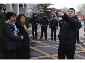 A Chinese security officer barks orders near relatives of passengers on board the missing Malaysia Airlines Flight 370 (MH370) who have gathered outside the Chinese Foreign Ministry demanding answers in Beijing, Friday, March 8, 2019. Friday marked the fifth anniversary of the disappearance of MH370, which vanished March 8, 2014 while en route from Kuala Lumpur to Beijing.