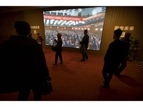 In this March 1, 2019, photo, people walk past a video display showing a meeting at the Great Hall of the People at an exhibition commemorating the 40th anniversary of China's Reform and Opening Up Movement at the National Museum in Beijing. China's ceremonial legislature is due to endorse a law Beijing hopes might help to defuse a bruising tariff war with Washington by discouraging officials from pressuring foreign companies to hand over technology. The fight with China's biggest trading partner is overshadowing the National People's Congress.