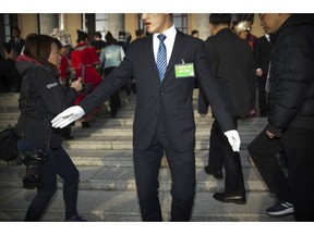 In this Tuesday, March 5, 2019 photo, a security official tries to keep journalists back from the steps of the Great Hall of the People as delegates arrive for the opening session of China's National People's Congress (NPC) in Beijing. The annual meeting of China's legislature is a highly scripted affair, but quirky moments and offbeat details lurk around the edges and behind the scenes.