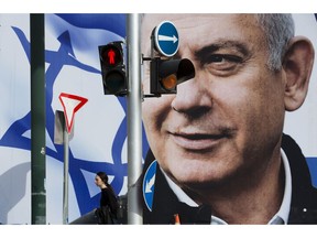 File - In this Thursday, March 28, 2019 file photo, a woman walks by an election campaign billboard showing Israel's Prime Minister Benjamin Netanyahu, the Likud party leader, in Tel Aviv, Israel. An Israeli watchdog said Monday that it's found a network of social media bots disseminating messages in support of Netanyahu ahead of next week's elections.