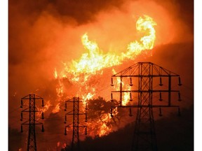 FILE - In this Dec. 16, 2017, file photo provided by the Santa Barbara County Fire Department, flames burn near power lines in Sycamore Canyon near West Mountain Drive in Montecito, Calif. A federal judge approved Pacific Gas & Electric Corp.'s plans Tuesday, April 23, 2019, to pay $235 million in employee bonuses this year, despite the California utility's bankruptcy and objections from lawyers of victims of the state's massive wildfires.