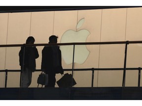 FILE - In this Jan. 3, 2019, file photo, shoppers pass by the Apple store logo at a shopping mall in Beijing. Apple Inc. reports financial results Tuesday, April 30.