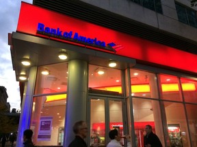 FILE- In this Nov. 6, 2017, file photo, people walk by a branch office of Bank of America in New York. Bank of America is raising its starting pay to $20 an hour over a two-year period, starting with a hike next month. The company said Tuesday, April 9, 2019, that it is raising its minimum hourly wage to $17 on May 1 and will continue to increase the pay until it hits $20 an hour in 2021.