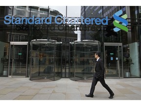 FILE - In this Aug 7, 2012, file photo a man walks by Standard Chartered bank in London. British financial services giant Standard Chartered Bank will pay $1.1 billion in fines to settle allegations by U.S. and British authorities that it attempted to evade U.S. sanctions imposed on Iran, Cuba, Burma and other nations. The settlement Tuesday,  April 9, 2019, was announced by the U.S. Treasury, the Federal Reserve and other bank regulators in the U.S. and Britain.