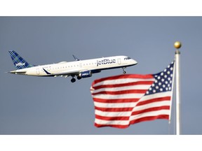FILE - In this Sept. 21, 2018, file photo, a plane flies past the American flag in Washington. JetBlue plans to join bigger rivals in offering flights between the US and Europe, starting with London in 2021. The move has been rumored for a long time, but the CEO says JetBlue has had to wait for a new Airbus plane that he says will make the flights economical.