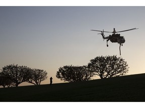 FILE - In this Nov. 11, 2018, file photo, a police officer takes pictures as a helicopter ascends after filling up its water tank at Pepperdine University, as firefighters continue to battle the Woolsey Fire in Malibu, Calif. Wildfires are more frequent and fierce. When people can't evacuate, some are sheltering in place. It's a dicey strategy for all but the fortunate.