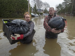 Residents Lawrence Courville (left) and Andie Goulet carry out belongings down a flooded street in Ste-Marthe-sur-le-Lac, Que., Sunday, April 28, 2019.