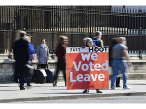 A supporter of Brexit holds a sign saying 'Just hoot, we voted leave' while others continue with their daily activities outside the Houses of Parliament in Westminster, London, ahead of the latest round of debates in the House of Commons concerning Brexit issues, Monday April 1, 2019.