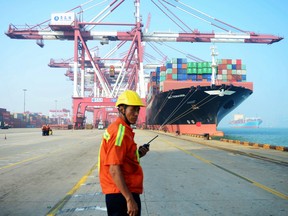 A Chinese worker looks on as a cargo ship is loaded at a port in Qingdao, china. The WTO report comes as Chinese Vice Premier Liu He visits Washington to continue talks aimed at ending the U.S.-China tensions.