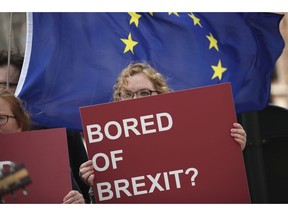 An anti-Brexit campaigner holds a sign in front of an EU flag during a protest outside EU headquarters in Brussels, Wednesday, April 10, 2019. European Union leaders meet Wednesday in Brussels for an emergency summit to discuss a new Brexit extension.