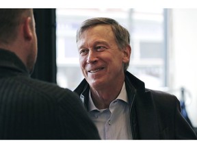 FILE - In this March 22, 2019, file photo, former Democratic Colorado Gov. John Hickenlooper talks with AmeriCorps members prior to a roundtable campaign stop in Manchester, N.H. Hickenlooper is proposing a $15 federal minimum wage _ with a twist. Rather than unilaterally hiking the national wage to $15, the former Colorado governor proposes phasing in the increases based on the cost of living.