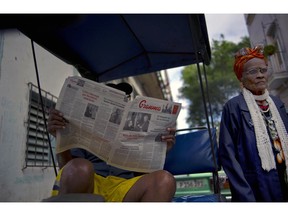 FILE - In this Feb. 3, 2015 file photo, a man reads a copy of the official newspaper of the Central Committee of the Cuban Communist Party, Granma, as a woman walks past, in old Havana. The Cuban government said on Thursday, April 4, 2019, that a newsprint shortage is forcing at least six state-run newspapers to cut back on pages and circulation days in a potent sign of the cash shortage confronting the island.