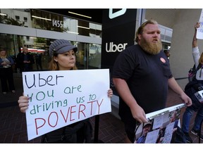 Annette Ribero, left, of San Jose, and Jeff Terry, of Sacramento, hold signs during a demonstration outside of Uber headquarters Wednesday, May 8, 2019, in San Francisco. As Uber executives lure investors to infuse the company with billions of dollars ahead of the largest technology IPO this year, the men and women behind the wheels of the largest ride-hailing companies are pushing for higher wages and recognition for their role in building the companies.