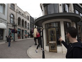 A woman climbs on a street sign to take pictures on Rodeo Drive in Beverly Hills, Calif., on Tuesday, May 7, 2019.