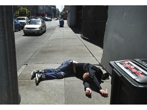 FILE - In this April 26, 2018, file photo, a man lies on the sidewalk beside a recyclable trash bin in San Francisco. A key federal count shows the number of homeless people increased by double-digit percentages in three San Francisco area counties over two years. In San Francisco, the number of homeless people jumped 17% to more than 8,000 in 2019.