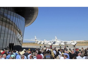 FILE - In this Oct. 17, 2011, file photo a crowd gathers outside Spaceport America for a dedication ceremony as Virgin Galactic's mothership WhiteKnightTwo sits on the tarmac near Upham, N.M. British billionaire Richard Branson is taking another concrete step toward offering rides into the close reaches of space for paying passengers. Branson announced Friday, May 10, 2019, that Virgin Galactic will immediately begin shifting operations from California to a spaceport and specialized runway in the New Mexico desert in final preparations for commercial flights. He says Virgin Galactic's development and testing program has advanced enough to make the move, which will continue through the summer.