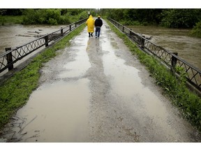 In this photo taken May 21, 2019, Robert Collins, left, and Bobby Joe Branston watch rising waters in the Fishing River from a condemned bridge in the small community of Mosby, Mo. Federal and local governments have poured more than $5 billion into buying tens of thousands of private properties over the past few decades to try to diminish the long-term costs of repeated floods.