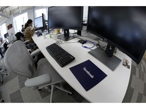 FILE- In this Jan. 9, 2019, file photo, Facebook employees sit at their stations during a tour of its new 130,000-square-foot offices in Cambridge, Mass. Facebook is raising what it pays U.S. contractors who do some of its most taxing work, including watching violent and other objectionable material for possible removal from the service. Facebook said Monday, May 13, that it will pay at least $18 an hour for these jobs.