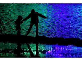 FILE - In this Nov. 30, 2018, file photo people are silhouetted against holiday lights reflecting off a pond in a park in Lenexa, Kan. Financial planning is daunting enough, but it becomes more complicated and critical when you have a child or family member with special needs. If you don't leave any money or support in place, their fate may be left up to the court and wellbeing could suffer.