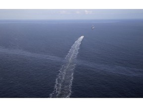 FILE - In this March 31, 2015 file photo, the wake of a supply vessel heading towards a working platform crosses over an oil sheen drifting from the site of the former Taylor Energy oil rig in the Gulf of Mexico, off the coast of Louisiana. The Coast Guard says a newly installed containment system is collecting oil at the site of the 14-year-old oil leak in the Gulf of Mexico.  A Coast Guard statement Thursday, May 16, 2019, describes the installation of the subsea containment system as a "major milestone" in the federal government's long-running efforts to contain the leak.