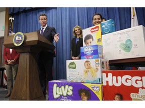 Gov. Gavin Newsom gestures towards boxes of tampons and diapers after proposing to eliminate from the state sales tax on such products in his upcoming state budget during a news conference, Tuesday, May 7, 2019, in Sacramento, Calif. The tax cuts are part of a "parents' agenda" Newsom is pursuing, and he plans to unveil a revised state budget later this week. Newsom was, accompanied by his wife, first partner Jennifer Siebel Newsom, center, Southern California Democratic Assemblywoman Monique Limon, right, and others.