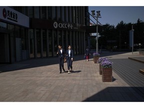 The sunlight is cast on women as they walk by a brokerage house in Beijing, Tuesday, May 7, 2019. Accusing Beijing of "reneging" on commitments it made in earlier talks, U.S. Trade Representative Robert Lighthizer says the Trump administration will increase tariffs on $200 billion in Chinese goods beginning Friday, a sharp escalation in a yearlong trade dispute.