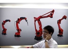 FILE - In this Aug. 15, 2018, file photo, a visitor talks on his smartphone in front of a display of manufacturing robots from a Chinese robot maker at the World Robot Conference in Beijing. In a report issued Monday, May 20, 2019, a business group says the number of foreign companies in China that feel compelled to hand over technology in exchange for market access has doubled since two years ago.