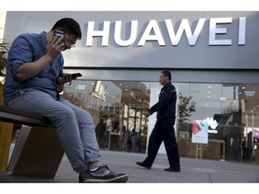 A man uses two smartphones at once outside a Huawei store in Beijing Monday, May 20, 2019. Google is assuring users of Huawei smartphones the American company's services still will work on them following U.S. government restrictions on doing business with the Chinese tech giant.
