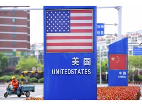 In this Wednesday, May 8, 2019, photo, a worker drives an electric cart past a display featuring the U.S. and Chinese flags in a special trade zone in Qingdao in eastern China's Shandong province. China said Thursday it will retaliate if President Donald Trump goes ahead with more tariff hikes in a fight over technology and trade, ratcheting up tensions ahead of negotiations in Washington. (Chinatopix via AP)