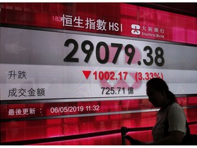 A woman walks past a bank's electronic board showing the Hong Kong share index at Hong Kong Stock Exchange Monday, May 6, 2019.  Shares tumbled in Asia early Monday after President Donald Trump threatened in a tweet to impose more tariffs on China, spooking investors who had been expecting good news on trade.