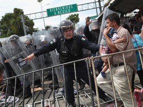 A Mexican riot policeman protects an immigrant father and child during a clash between police and the migrant caravan on the border between Mexico and Guatemala on October 19, 2018 in Ciudad Tecun Uman, Guatemala.