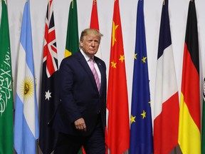 U.S. President Donald Trump walks past G20 member flags as he is welcomed by Japanese Prime Minister Shinzo Abe prior to the family photo at the G20 Osaka Summit in Osaka on June 28, 2019.