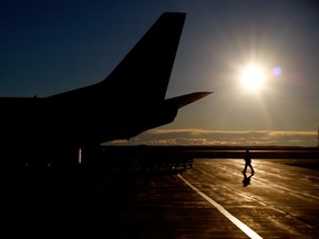 An attendant and a Flair Airlines Boeing 737-400 charter airplane are silhouetted on the Grande Prairie Airport tarmac on Tuesday, Nov. 4, 2014 in Grande Prairie, Alberta.