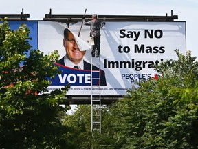 A worker removes a billboard featuring the portrait of People’s Party of Canada (PPC) leader Maxime Bernier and its message "Say NO to Mass Immigration" in Toronto, Ontario, on August 26, 2019.