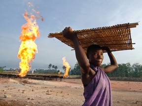 A woman carries tapioca seeds next to a gas flare fire, near the Niger Delta port city of Warri. Nigeria, Africa's largest oil exporter relies on oil for some two-thirds of its revenue.