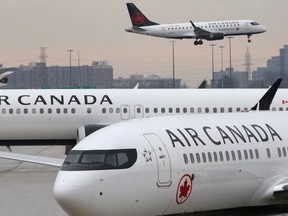 Two Air Canada Boeing 737 MAX 8 aircrafts seen on the ground as Air Canada Embraer aircraft flies in the background at Toronto Pearson International Airport.