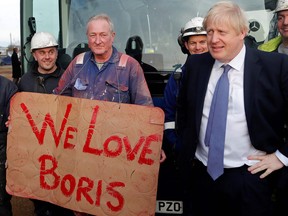 Britain's Prime Minister Boris Johnson reacts ashe poses with workers holding a "We Love Boris" sign during a general election campaign visit to Wilton Engineering Services, in Middlesbrough, north-east England on November 20, 2019.