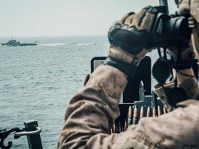 A U.S. Marine observes an Iranian fast attack craft in the Strait of Hormuz off Oman, in July 2019. The strait is a chokepoint for about a third of the world's sea-borne oil.