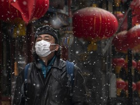 Chinese man wears a protective mask as he walks during a snowfall in an empty and shuttered commercial street on February 5, 2020 in Beijing, China.